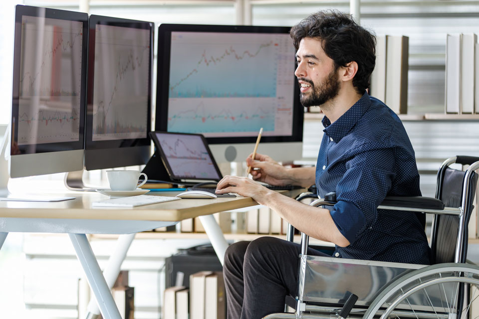 Smiling caucasian male investor who uses a wheelchair typing information on computer