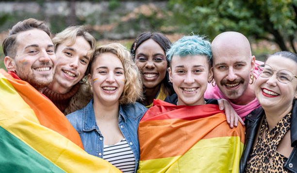 a multi-ethnic group of people wrapped in a Pride flag.