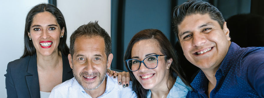 Smiling Hispanic colleagues taking a selfie in the office.