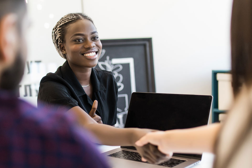 A young Black woman smiles while shaking hands.