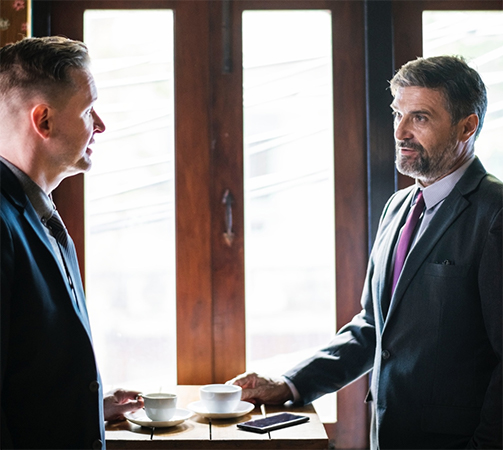Two men, in business attire, having a conversation over coffee.
