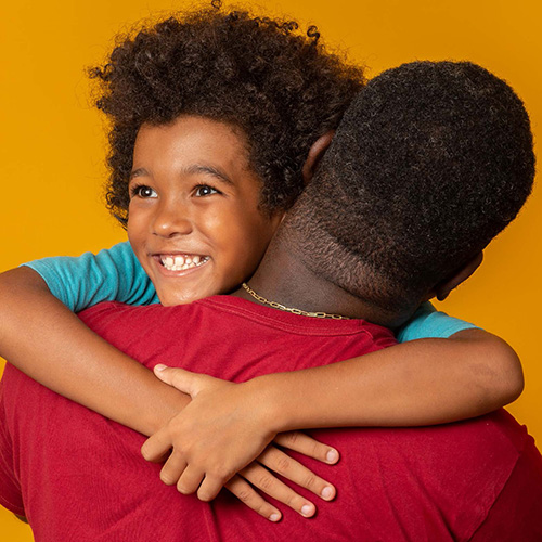 Black man hugging a smiling black boy.