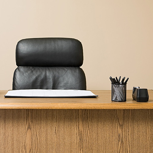 An unoccupied desk with a black executive chair and a stack of paper on the left