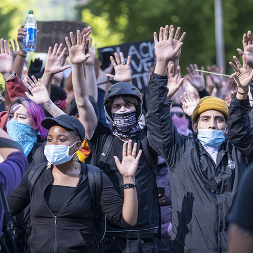 Group of masked protestors wearing black with their hands up