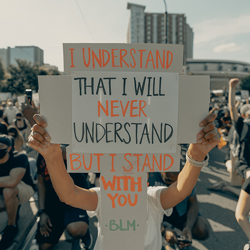 Individual holding a sign that read I understand that I will never understand, but I stand with you. -BLM