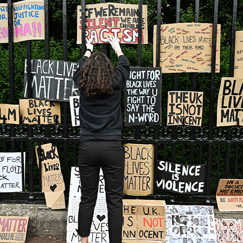 A woman displaying a BLM protest sign on a fence with other BLM protest signs.