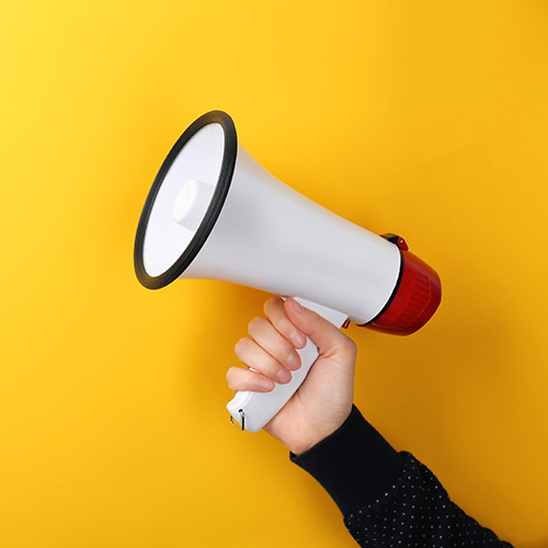 A hand holding a white megaphone against a yellow background