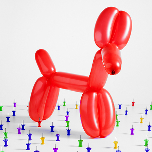 A red balloon dog in the on a table full of upright pushpins