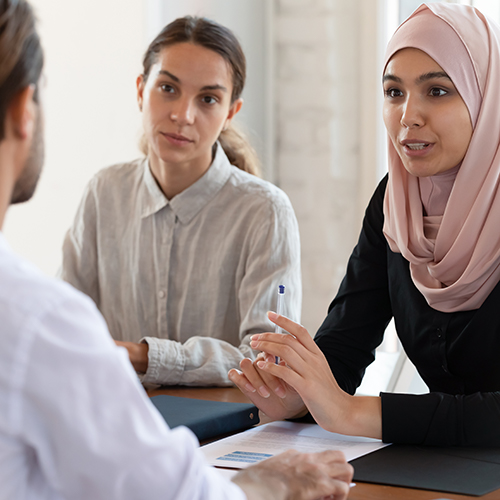 A white woman, and woman wearing a hijab, and a white male having a discussion