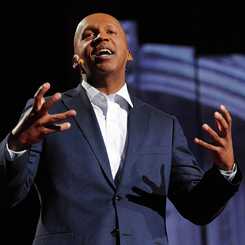 A bald black man in a blue suit giving a speech