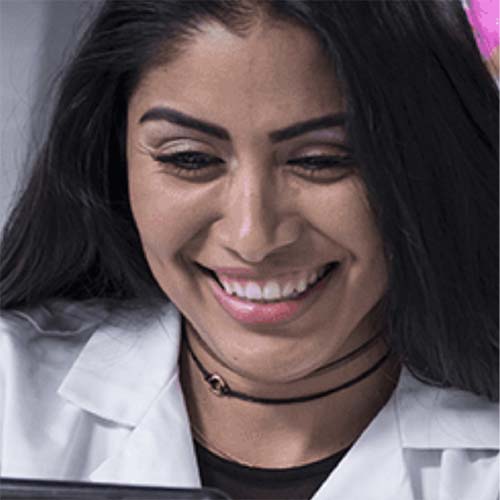 A young woman with a smile on her face wearing a lab coat.