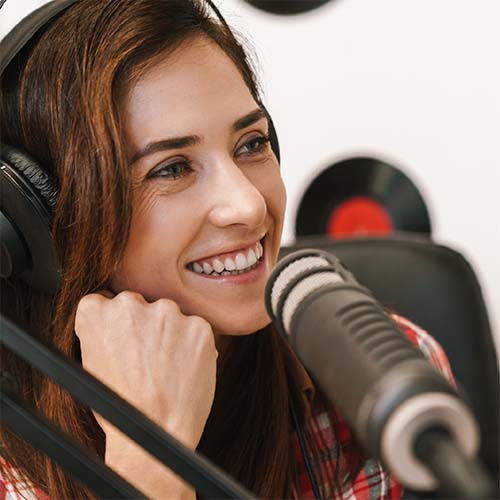 A young lady with headphones on sitting in front of a mic.
