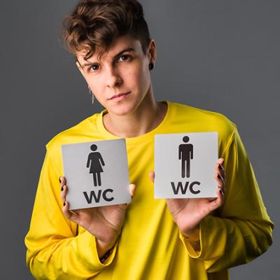 Image of a person in a yellow shirt holding two gendered bathroom signs.