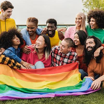 A diverse group of friends hold a pride flag while smiling and now fun outdoors.
