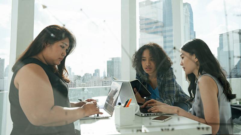 Three women of color working together in a brightly sunlit office.