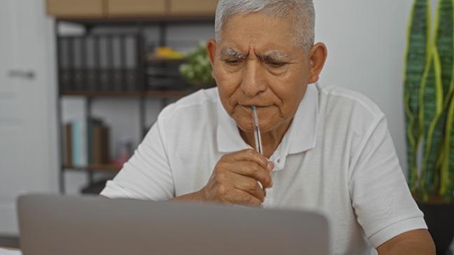 An older Hispanic man looking at his laptop computer. 